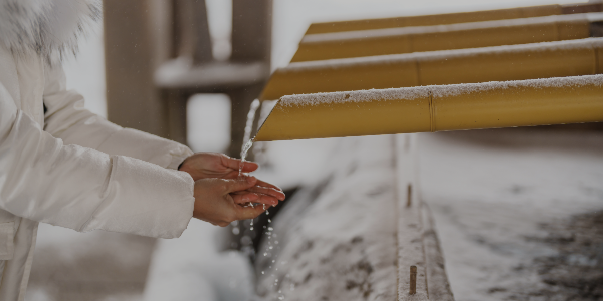 Snowy outdoor scene with outdoor handwashing station. A woman in a puffy winter coat washes her hands.